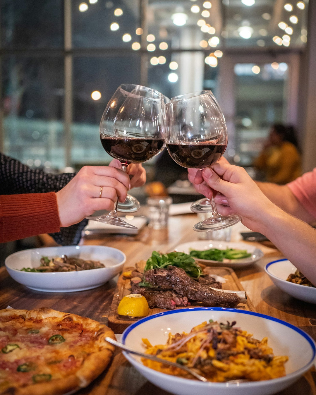 Two people clinking glasses of red wine over a dinner party table