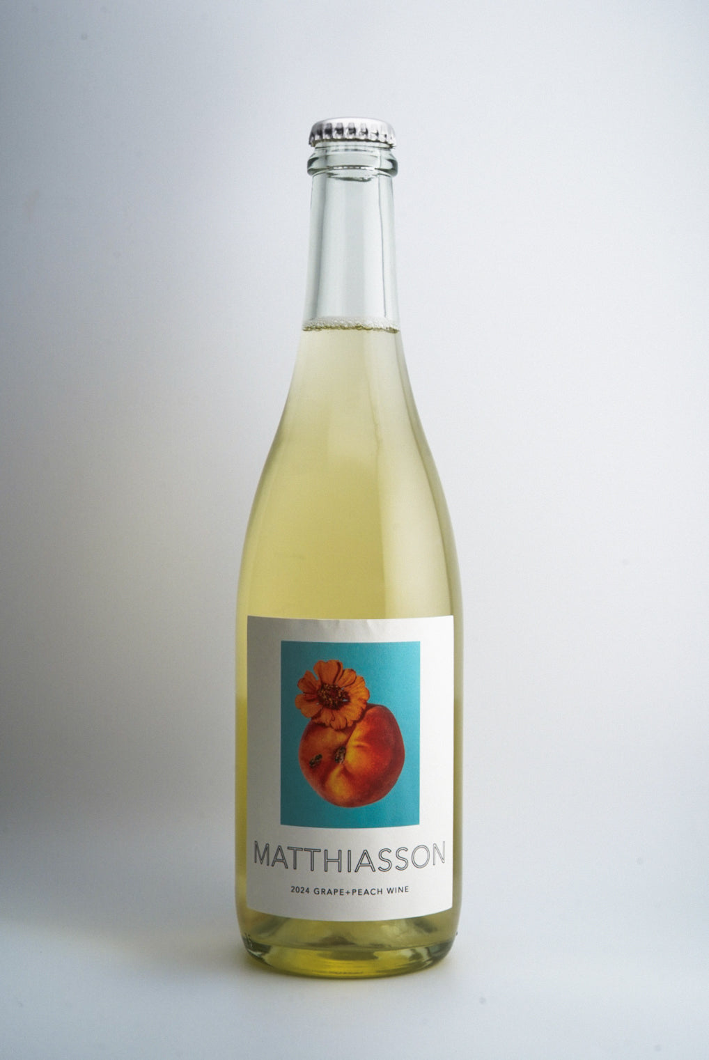 A bottle of Matthiasson Peach + Grape Sparkling Wine with a label featuring an image of a peach. The background is plain and white.