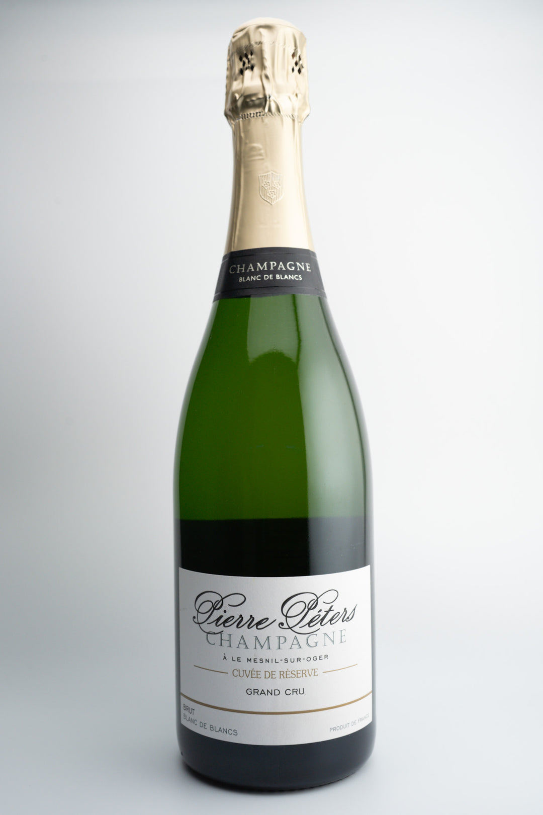 A bottle of Pierre Péters 'Cuvee de Reserve' Blanc de Blancs Grand Cru Brut Champagne with a celebratory label on top.